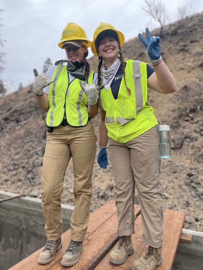 Two WCC members smile at the camera while standing on top of a wooden wildlife crossing over a canal.